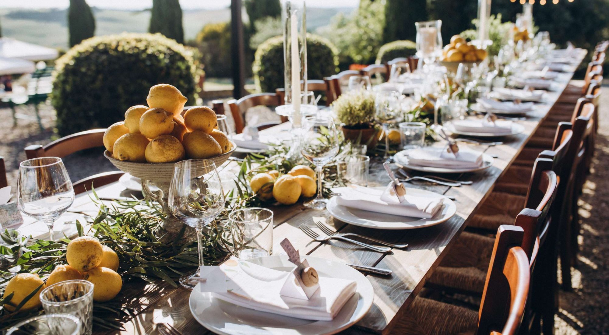 in the back yard of the old villa there is a long festive table, which is decorated with lemons and herbs, on the table are plates, glasses and candles. Wedding in Italy. Tuscany